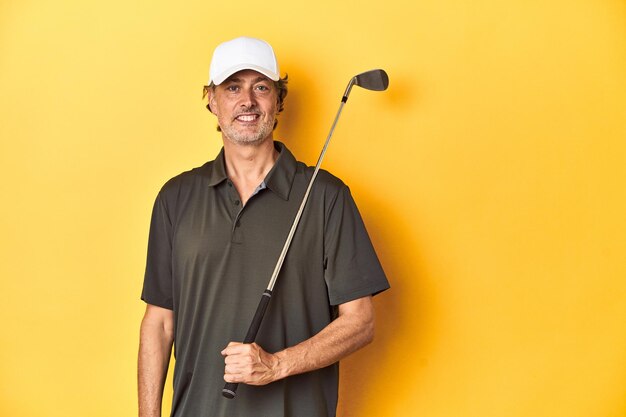 Middleaged golfer with club and cap on yellow happy smiling and cheerful