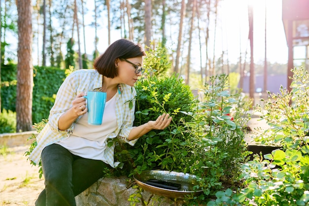 손에 컵을 들고 정원에서 휴식을 취하는 중년의 행복한 여성