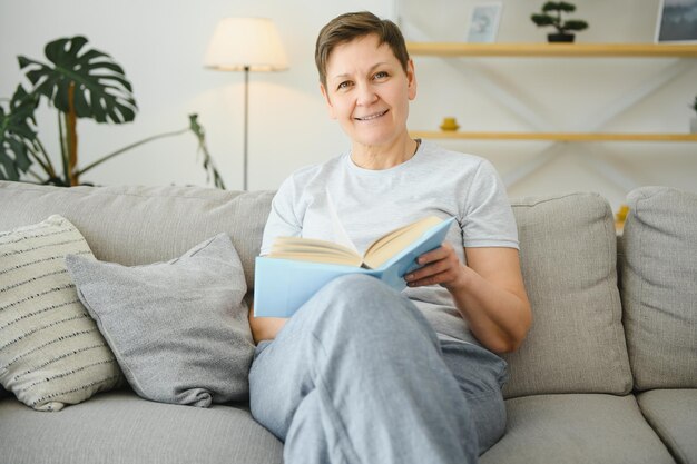 Middleaged housewife sitting on sofa with book free time retirement hobby