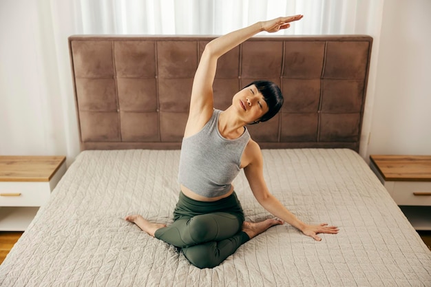 A middleaged japanese woman is practicing yoga in bedroom in fire log pose