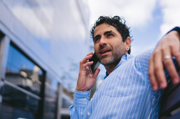 オフィスの外で電話で取引を交渉するシャツを着た中年のラテン系ビジネスマンコピースペース