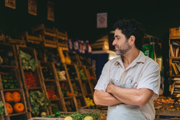 Латинский овощевод средних лет, стоящий перед своим бизнесом со скрещенными руками и гордым выражением лица