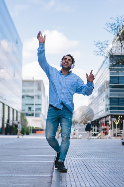 Middleaged Latin man dancing in the street with his arms raised and wearing headphones Vertical photo