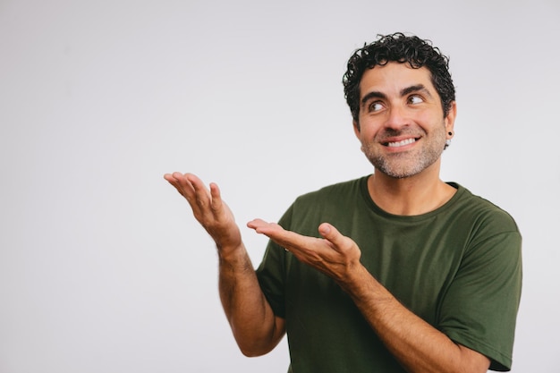 Латиноамериканец средних лет, указывающий обеими руками в сторону с улыбкой на белом фоне