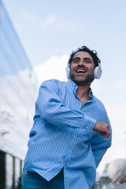 Middleaged latin man walking happily through the city while wearing headphones Vertical photo