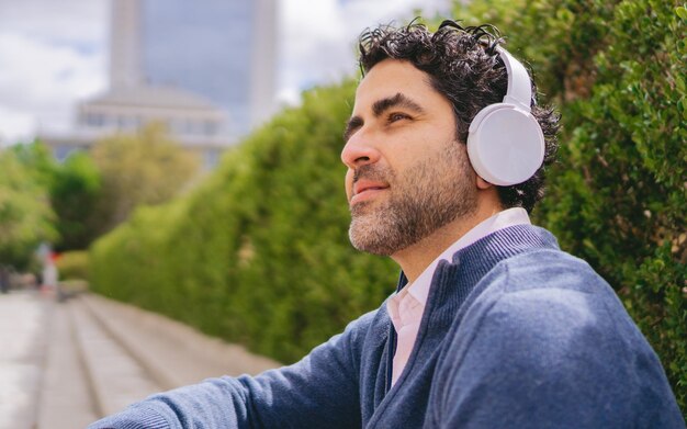 都市の歩道で休んでいる間にヘッドフォンを着用した中年のラテン人男性 コピースペース