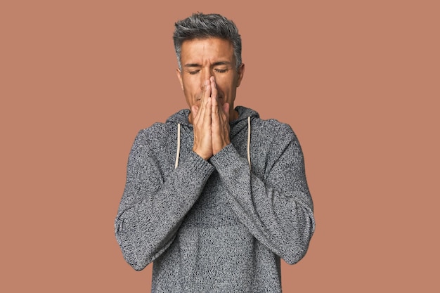 Middleaged Latino man holding hands in pray near mouth feels confident