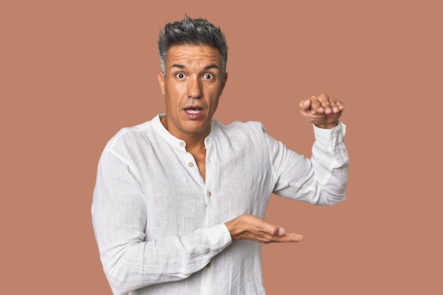 Middleaged Latino man shocked and amazed holding a copy space between hands