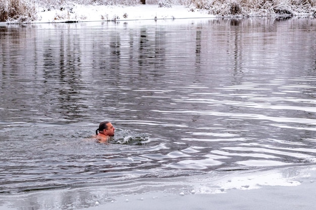 雪に覆われた木々を背景に冬の川で水浴びをする中年男性 健康的なライフスタイルを強化するというコンセプト 洗礼のための入浴