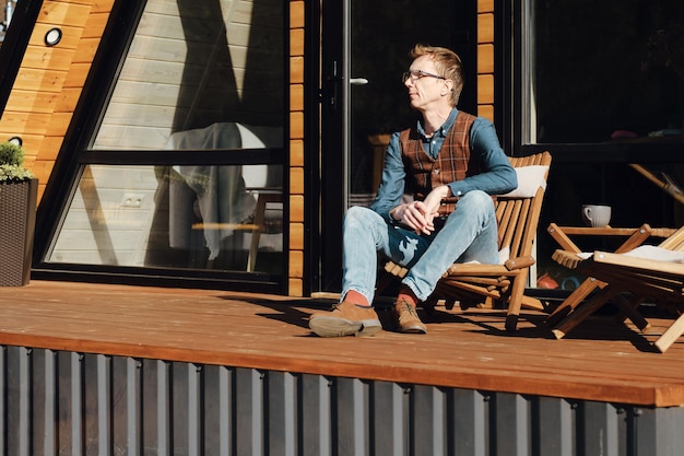 Middleaged man enjoys warm autumn morning sitting on terrace of summer house