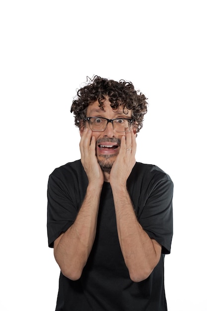 Middleaged man holding his face with his hands with a terrified expression on a white background