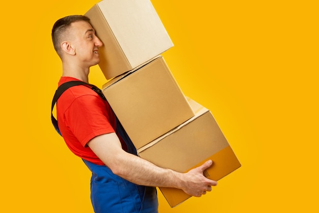 Middleaged man moves holds several large boxes loader carries heavy boxes isolated on yellow background copy space mock up