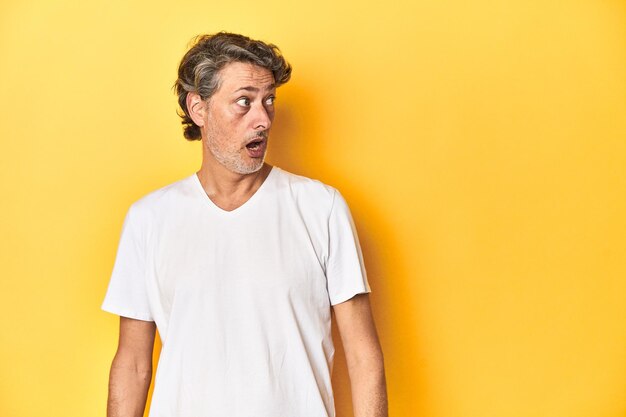 Middleaged man posing on a yellow backdrop being shocked because of something she has seen