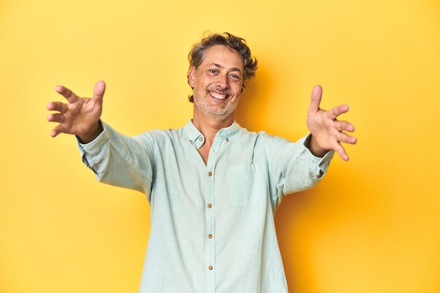 Photo middleaged man posing on a yellow backdrop feels confident giving a hug to the camera