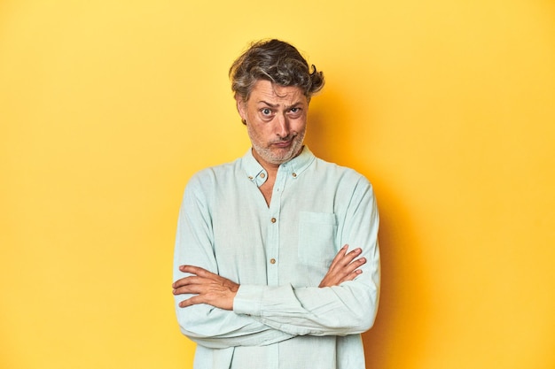 Photo middleaged man posing on a yellow backdrop unhappy looking in camera with sarcastic expression