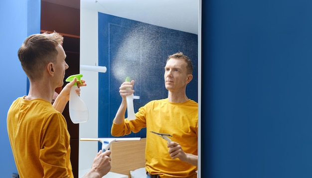 Middleaged man spraying cleaning liquid on mirror at home