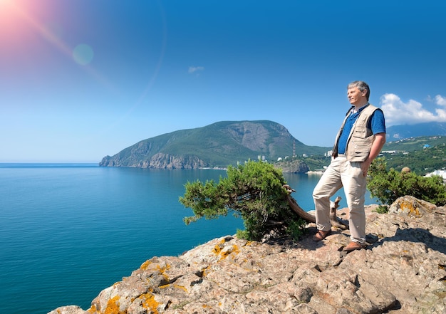 A middleaged man stands on a rock above the sea