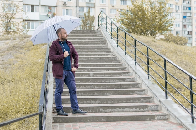 A middleaged man with a beard on the stairs under an umbrella