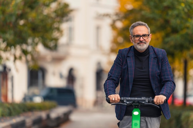 Middleaged man with grey hair and beard smiling looking at camera riding rental electric scooter