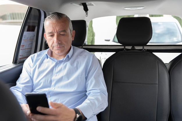 A middleaged passenger sitting in the backseat of a cab looking\
at his mobile phone