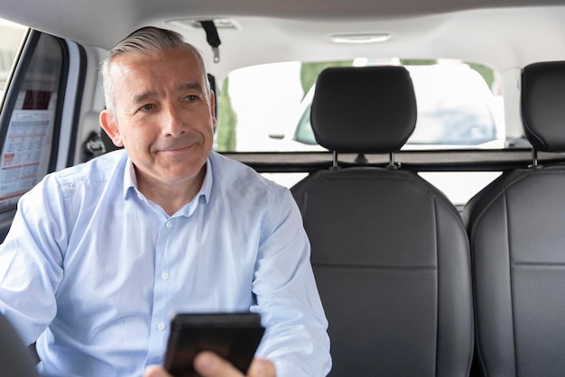 A middleaged passenger sitting in the backseat of a cab looking at his mobile phone