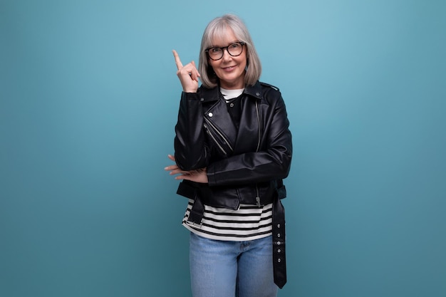 Middleaged pensioner woman in gray hair in a stylish youth look points her finger to the side on a