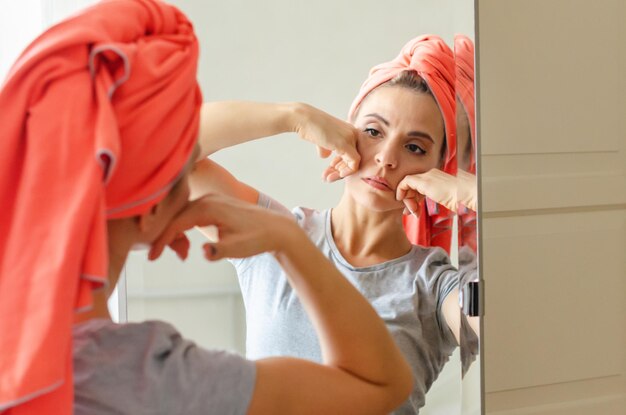 Middleaged woman doing face building exercises at home massaging her face beauty routine Spa wellness skincare Female doing routine self care at mirror taking care of facial skin by massage