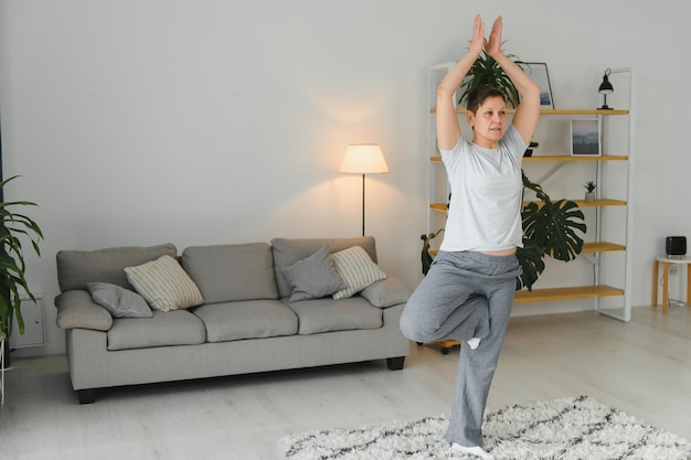 Middleaged woman doing yoga at home for stretching and being healthy