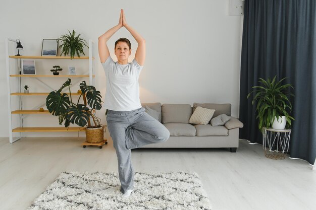 Middleaged woman doing yoga at home for stretching and being healthy