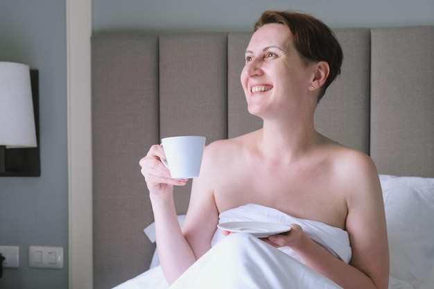 Middleaged woman drinks coffee in bed Woman is resting in a hotel and relaxing