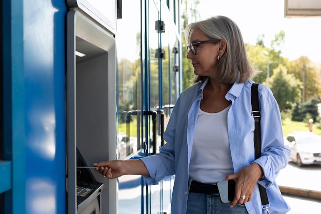 Женщина средних лет спешит снять наличные в банкомате на улице