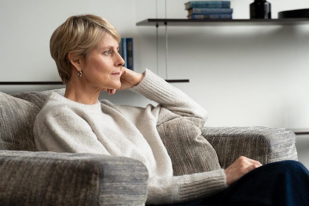 A middleaged woman is sitting alone in an armchair and looking at the view from the window