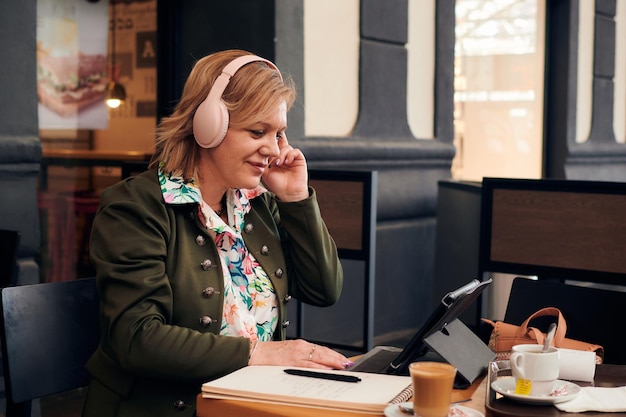 Middleaged woman listens to music and looks at a tablet in a coffee shop