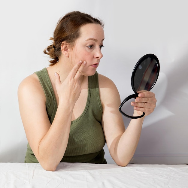 Photo a middleaged woman looks worriedly at herself in the mirror