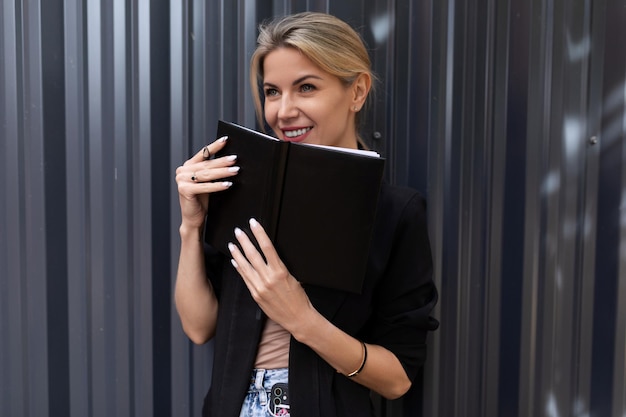 Офисная работница средних лет держит ноутбук с улыбкой и смотрит в камеру