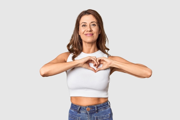 Middleaged woman portrait in studio setting smiling and showing a heart shape with hands