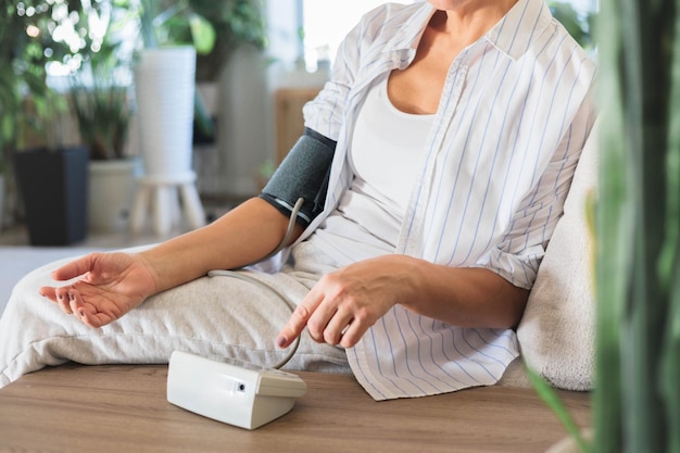 a middleaged woman sits on the couch and measures her own blood pressure concept hypertension