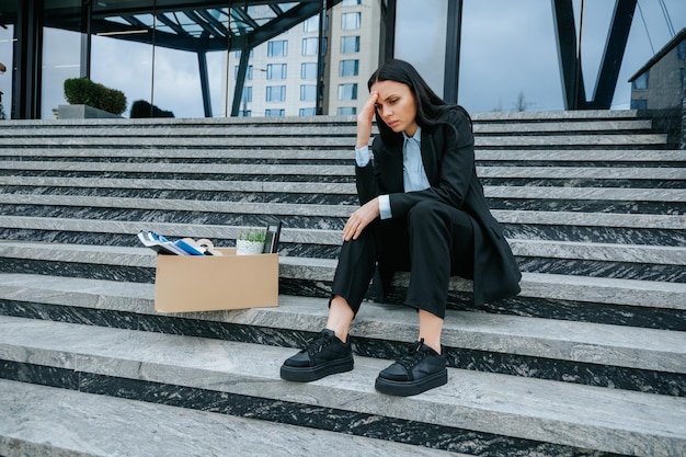 Photo a middleaged woman sits on the stairs with a sign reading fired from my job please help feeling the effects of her work loss and unemployment