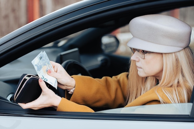 中年の女性が車のハンドルの後ろに座って、駐車料金を支払うために財布の中からユーロを探す