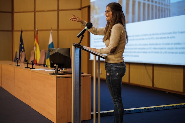 Middleaged woman standing on the lectern to give a speech to her students during her graduation Concept Education teachers coaching