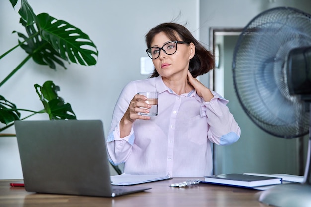 Middleaged woman suffering from heat overheated cooled by fan and fan