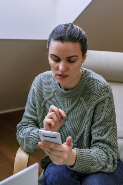 middleaged woman in a sweater does sitting in a chair at home communication via video call
