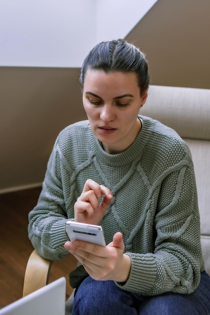 Photo middleaged woman in a sweater does sitting in a chair at home communication via video call