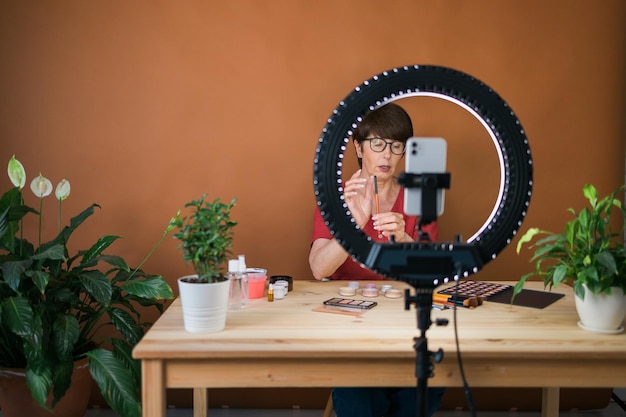 Middleaged woman talking on cosmetics with makeup eye shadows and blush palette and brushes while recording her video Mature female making video for her blog on cosmetics