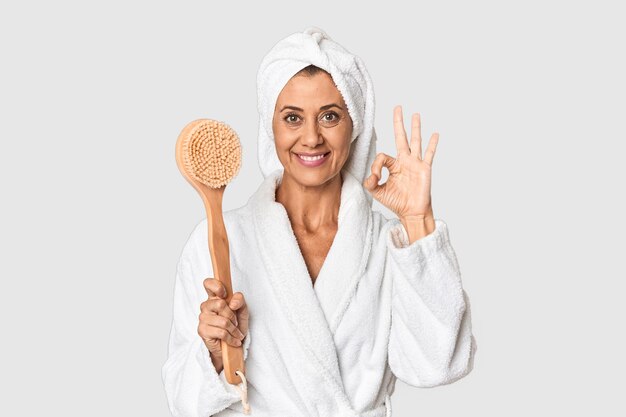 Photo middleaged woman with backscratcher in studio cheerful and confident showing ok gesture