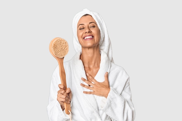 Photo middleaged woman with backscratcher in studio laughs out loudly keeping hand on chest