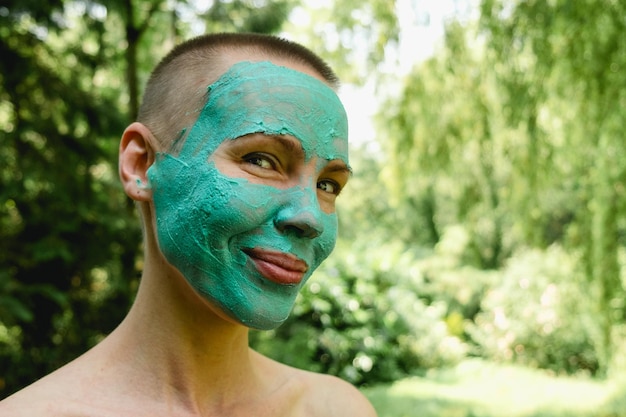 A middleaged woman with a short haircut wearing a green cosmetic mask against a background of trees Freshness rejuvenation concept