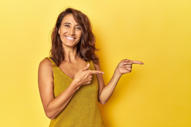 Foto donna di mezza età su uno sfondo giallo eccitata che punta con le dita indice via