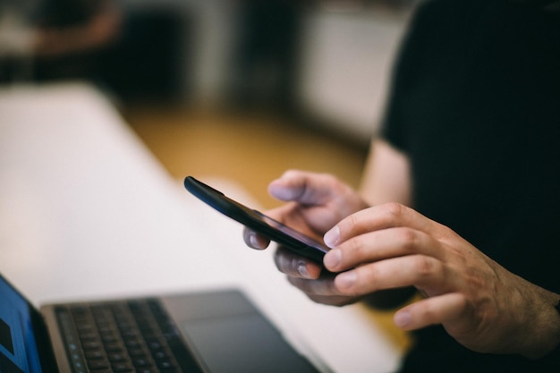 Midsectie van een man die een mobiele telefoon gebruikt met een laptop aan tafel in het kantoor