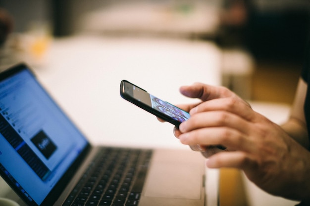 Midsectie van een man die een mobiele telefoon gebruikt met een laptop aan tafel in het kantoor